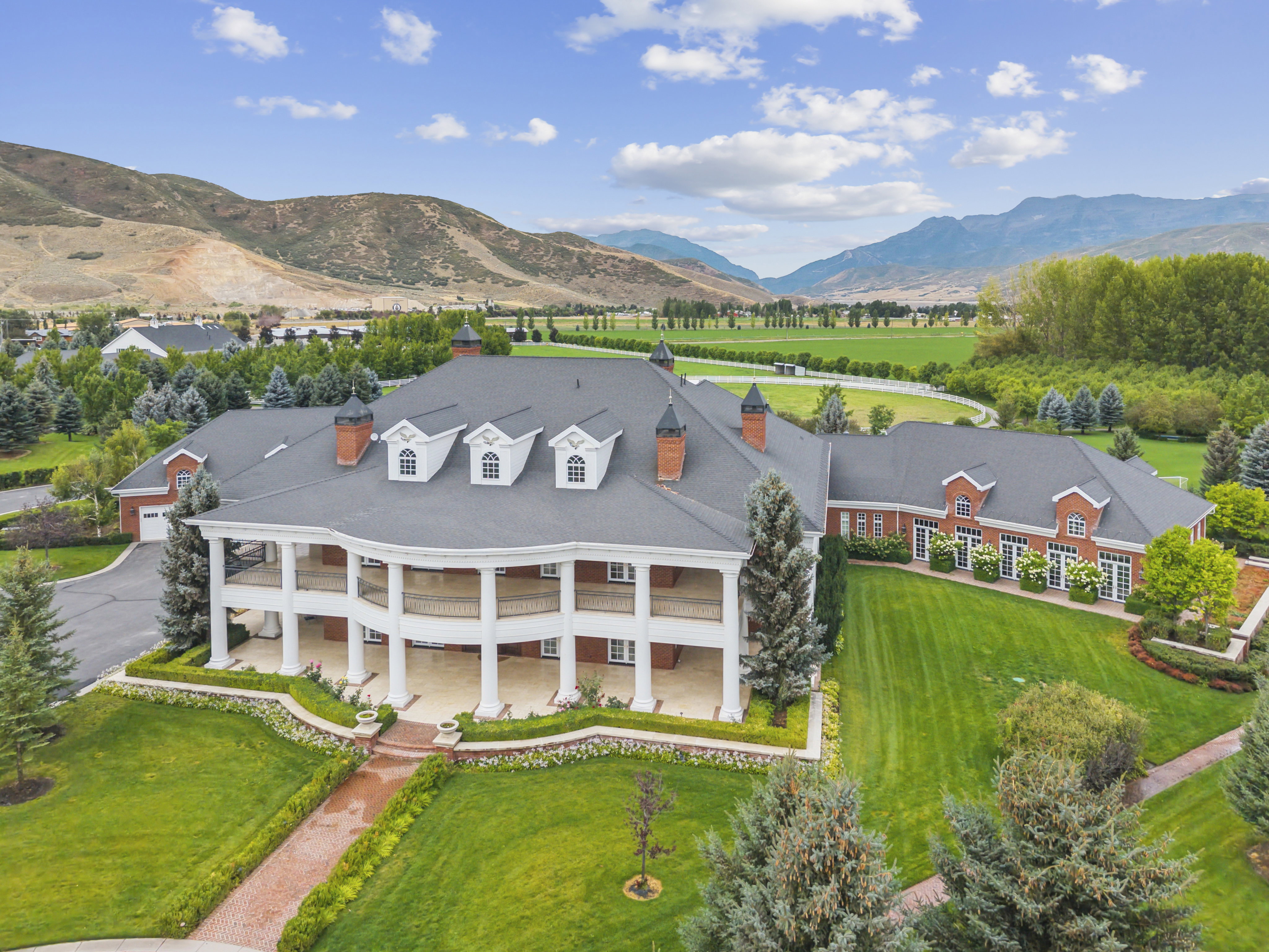 Expansive estate featuring a red brick exterior with white trim, a multi-level wrap-around porch, mature landscaping, a paved driveway, and mountain scenery