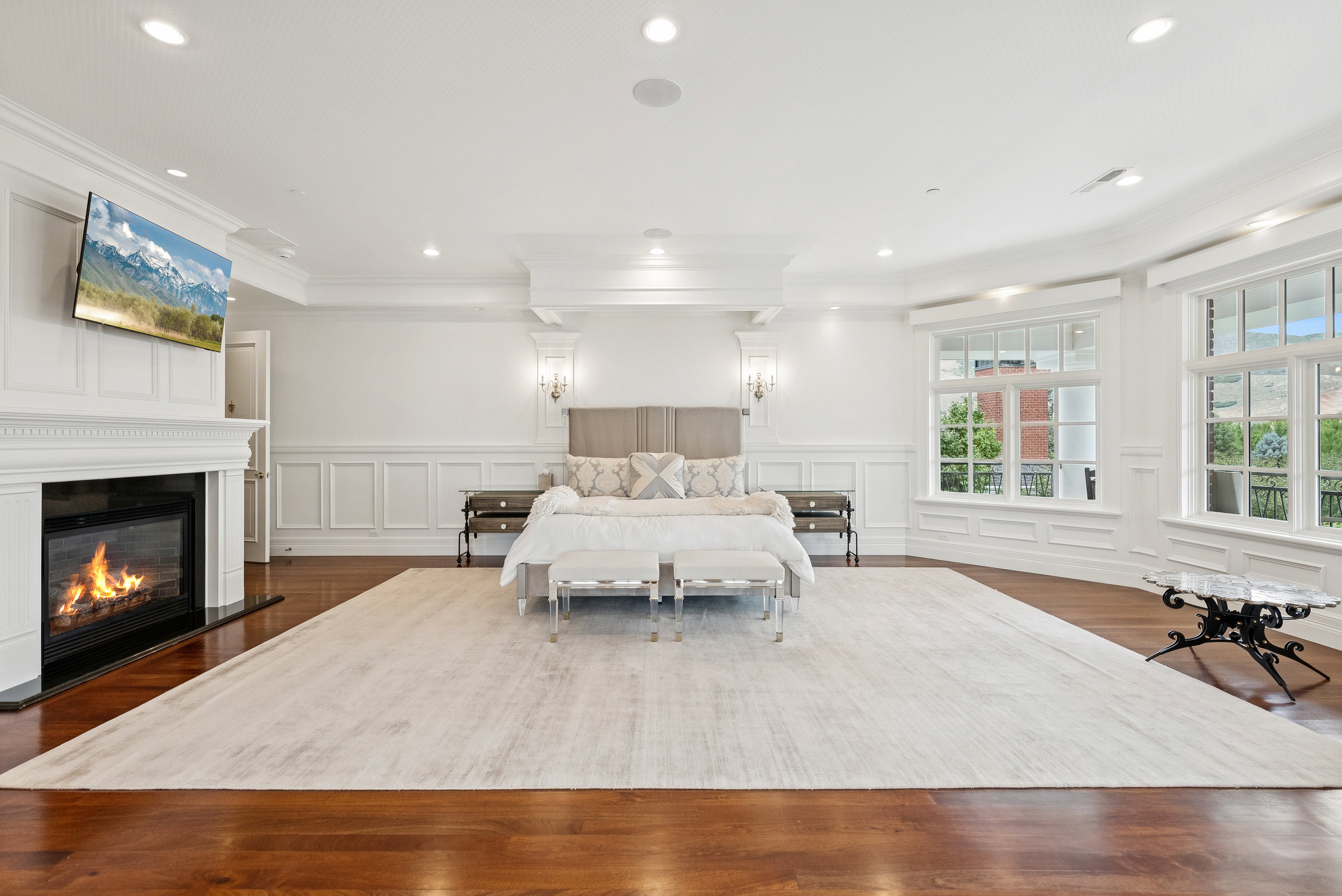 Spacious room featuring hardwood flooring, extensive white wainscoting, an integrated fireplace with a traditional mantel, recessed lighting, and multiple large windows