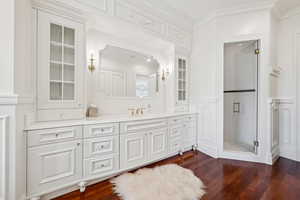 Full bath featuring vanity, ornamental molding, dark wood-type flooring, a stall shower, and a decorative wall