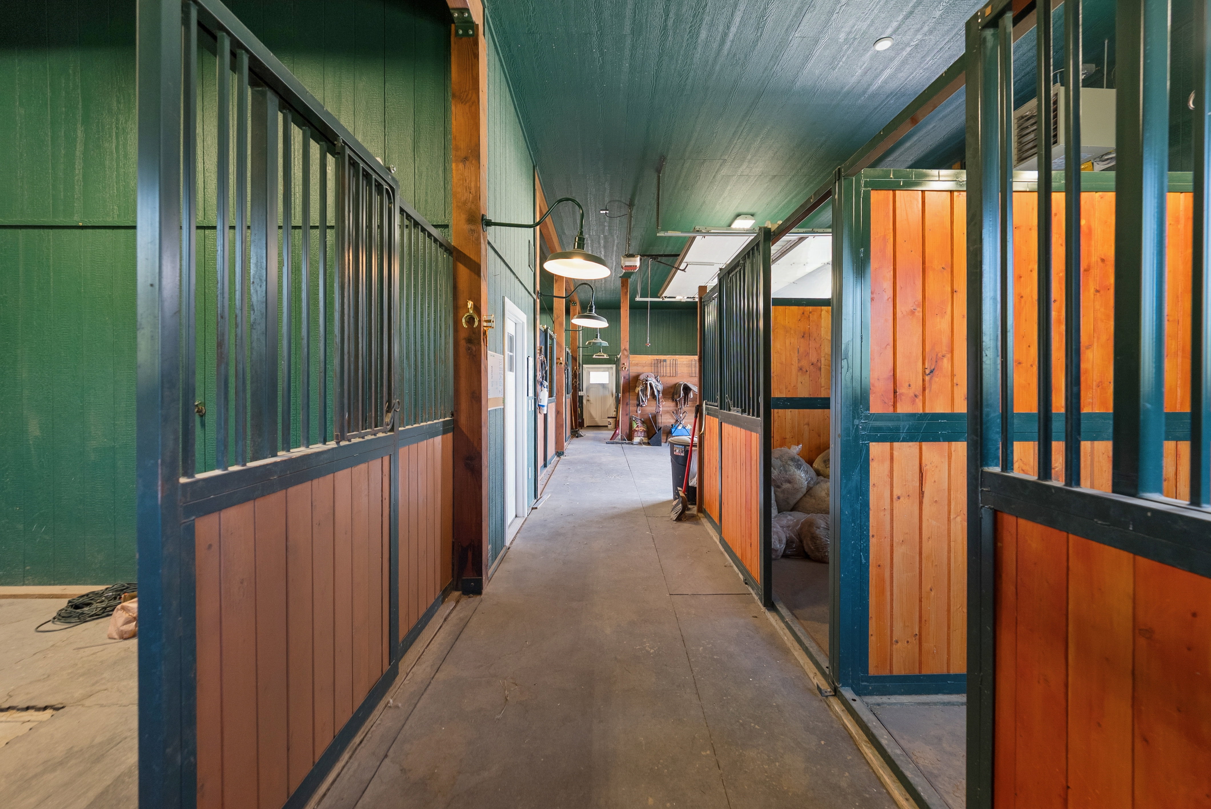 Barn interior featuring multiple stalls with wood-finish paneling and metal bars
