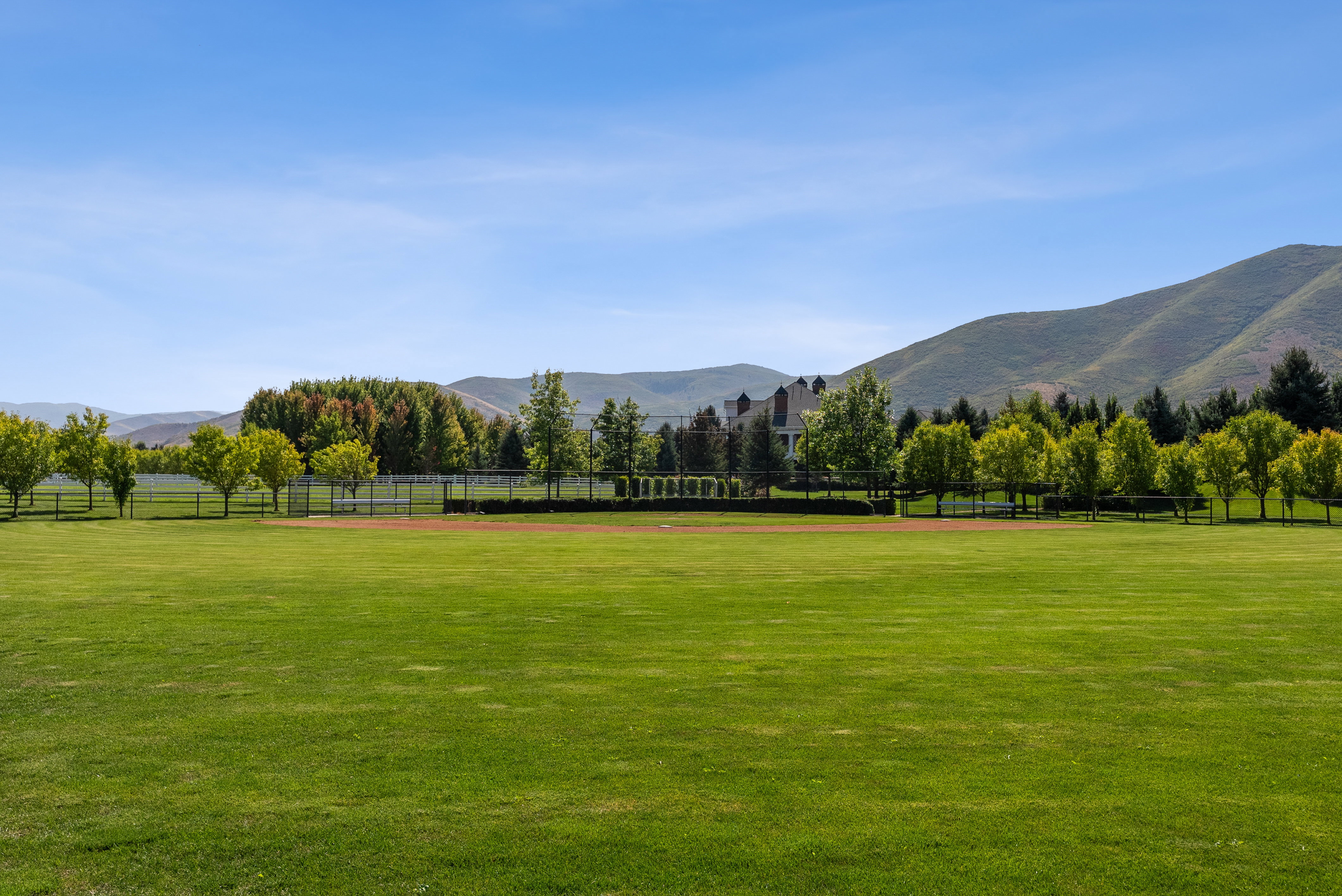 Expansive green lawn with a tree-lined perimeter and a mountain backdrop