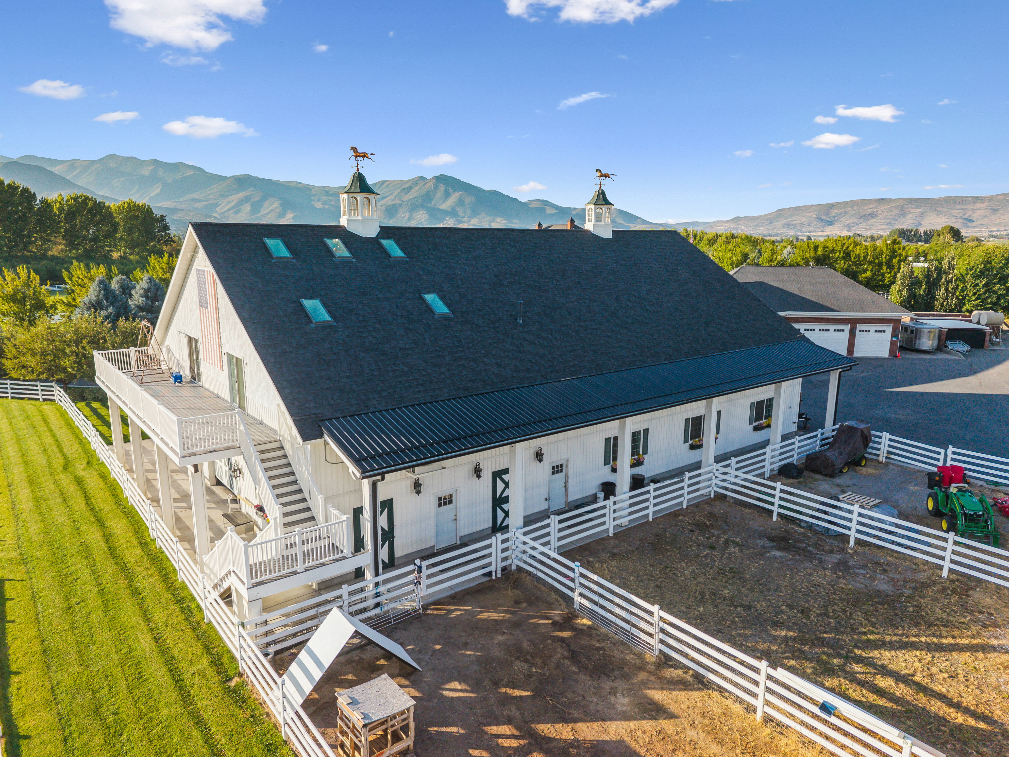 White barn structure featuring a dark shingle roof with skylights and two cupolas with horse weathervanes