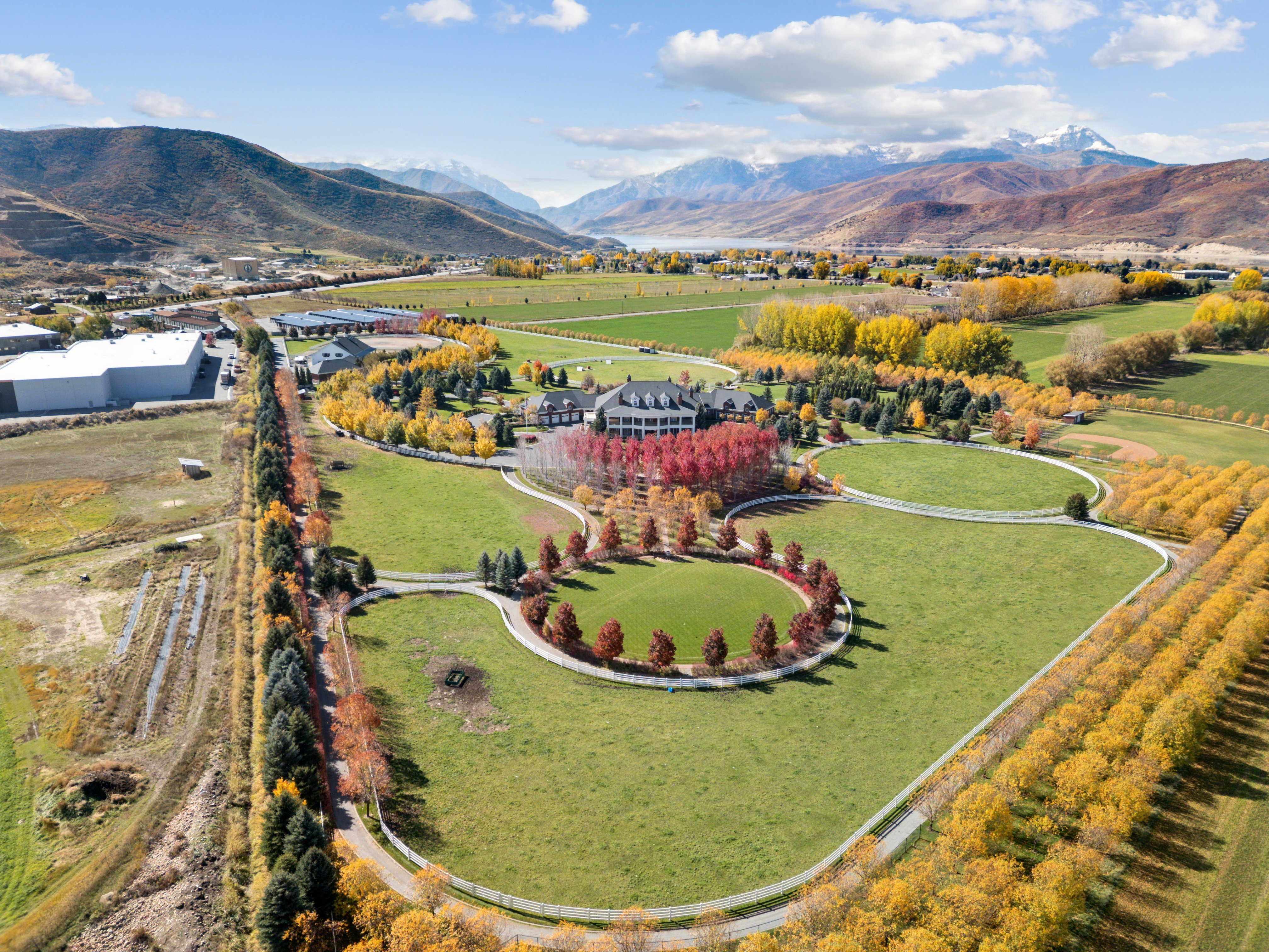 Extensive property featuring a large estate house, multiple outbuildings, vast green lawns, mature trees, and a mountain backdrop