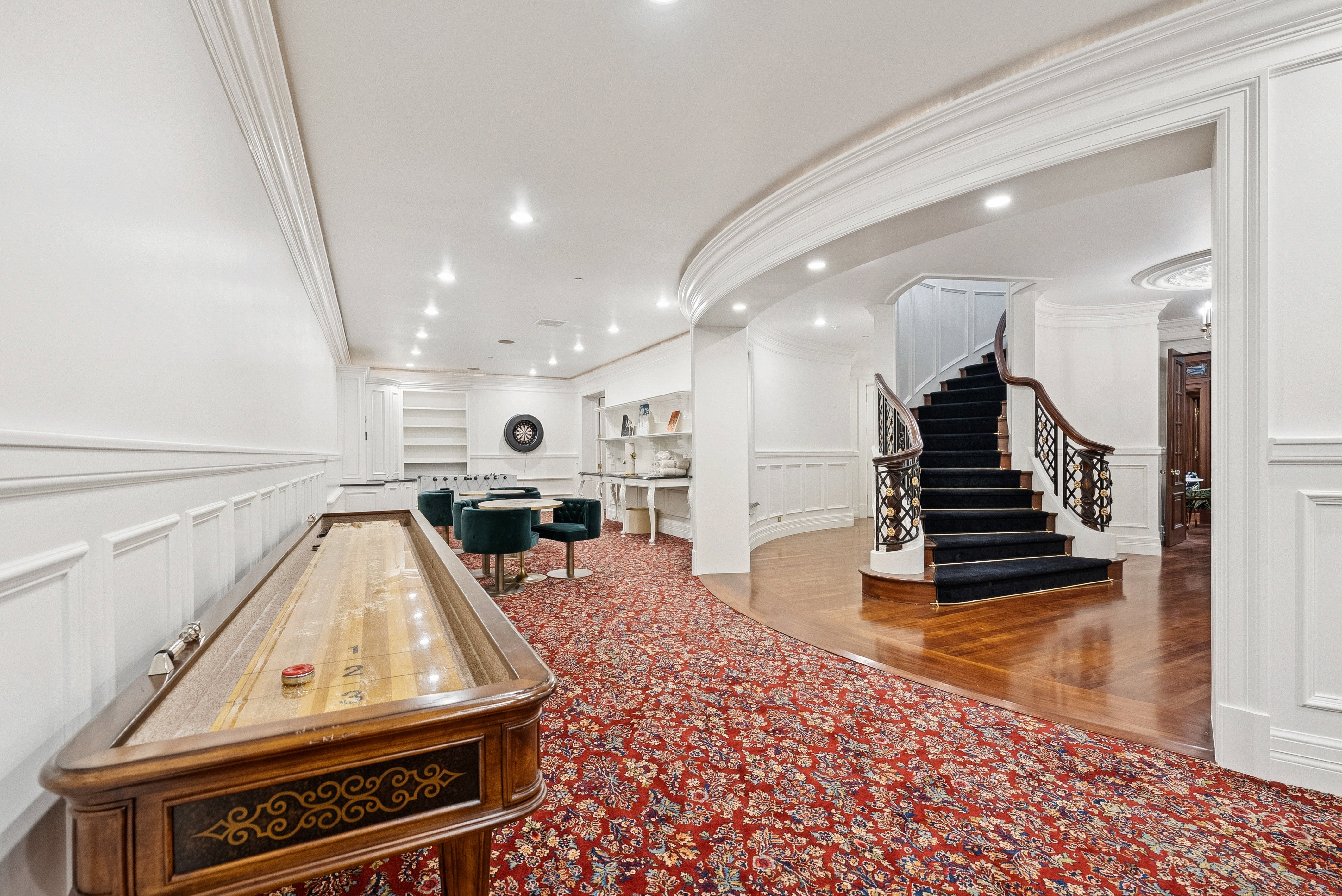 Expansive lower level featuring a grand curved staircase with intricate wrought iron balusters, hardwood flooring, recessed lighting, and elegant crown molding and wainscoting