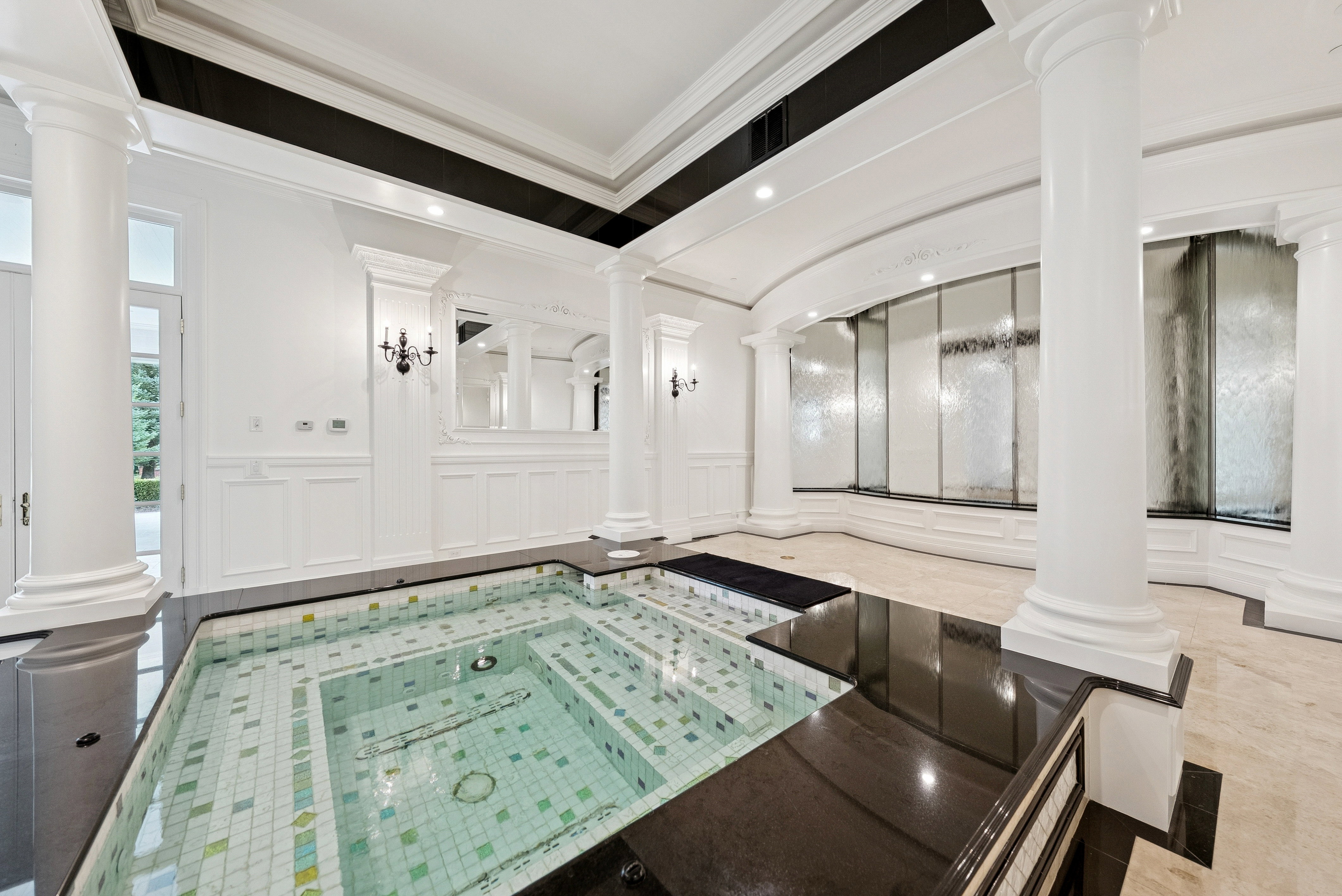 Indoor tiled spa with dark perimeter surfacing, flanked by ornate white columns and wainscoting
