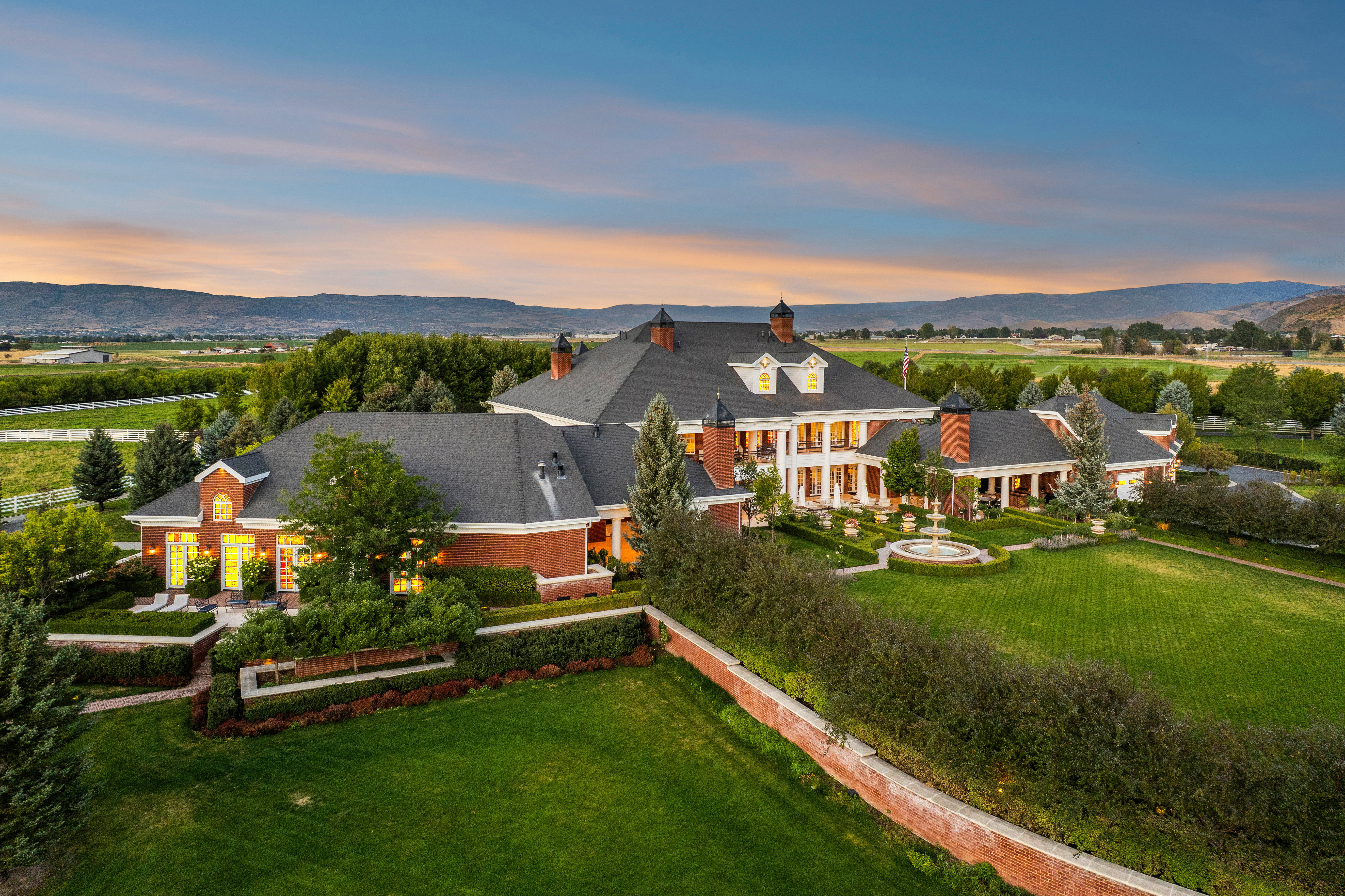 Expansive estate featuring a red brick exterior, multiple gabled roofs, and a symmetrical facade with white columns
