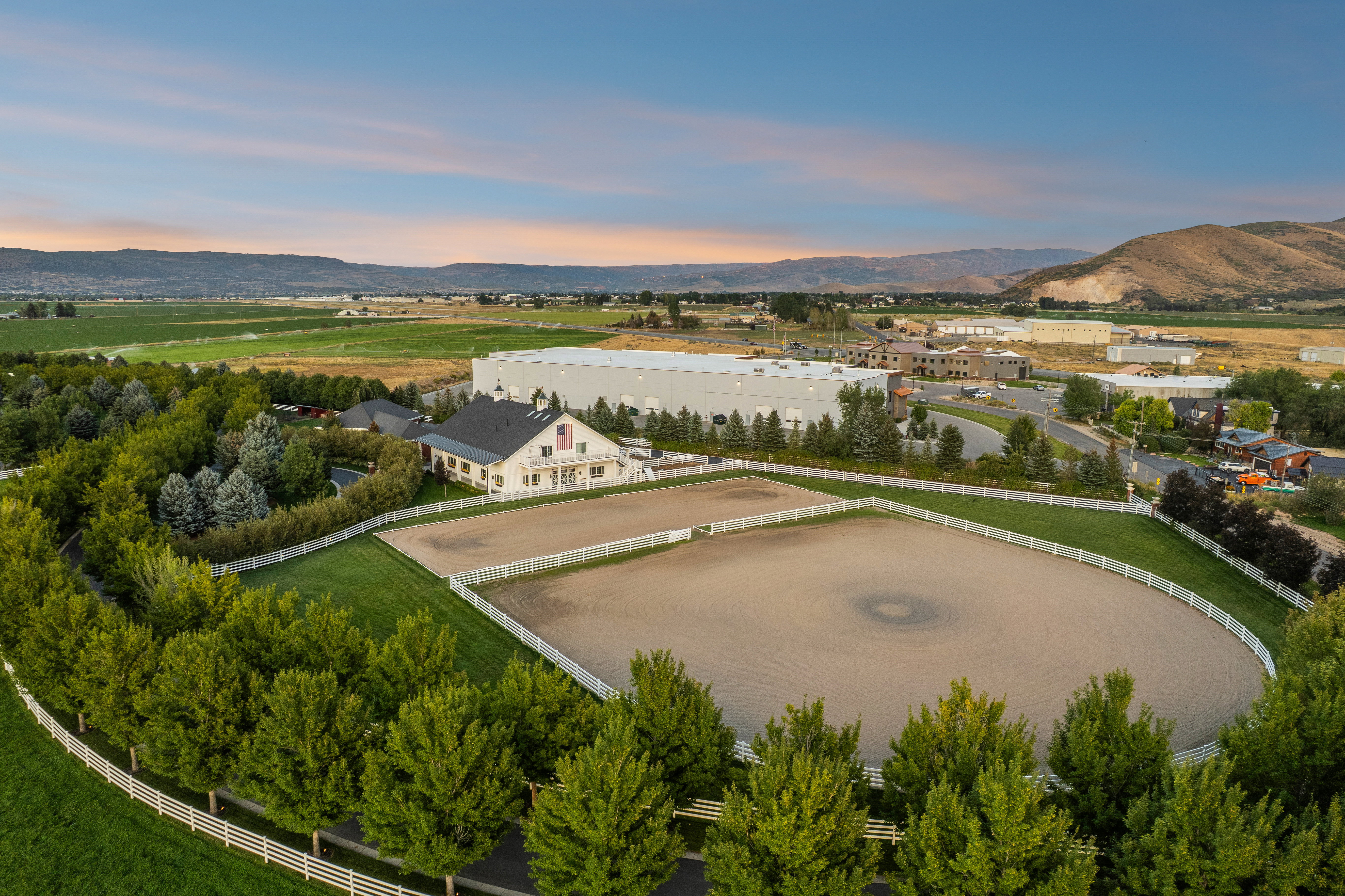 Expansive equestrian property featuring a large arena with white fencing, a manicured lawn, and mature trees