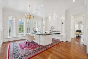 Dining area featuring a decorative wall, ornamental molding, dark wood-style flooring, a chandelier, and recessed lighting
