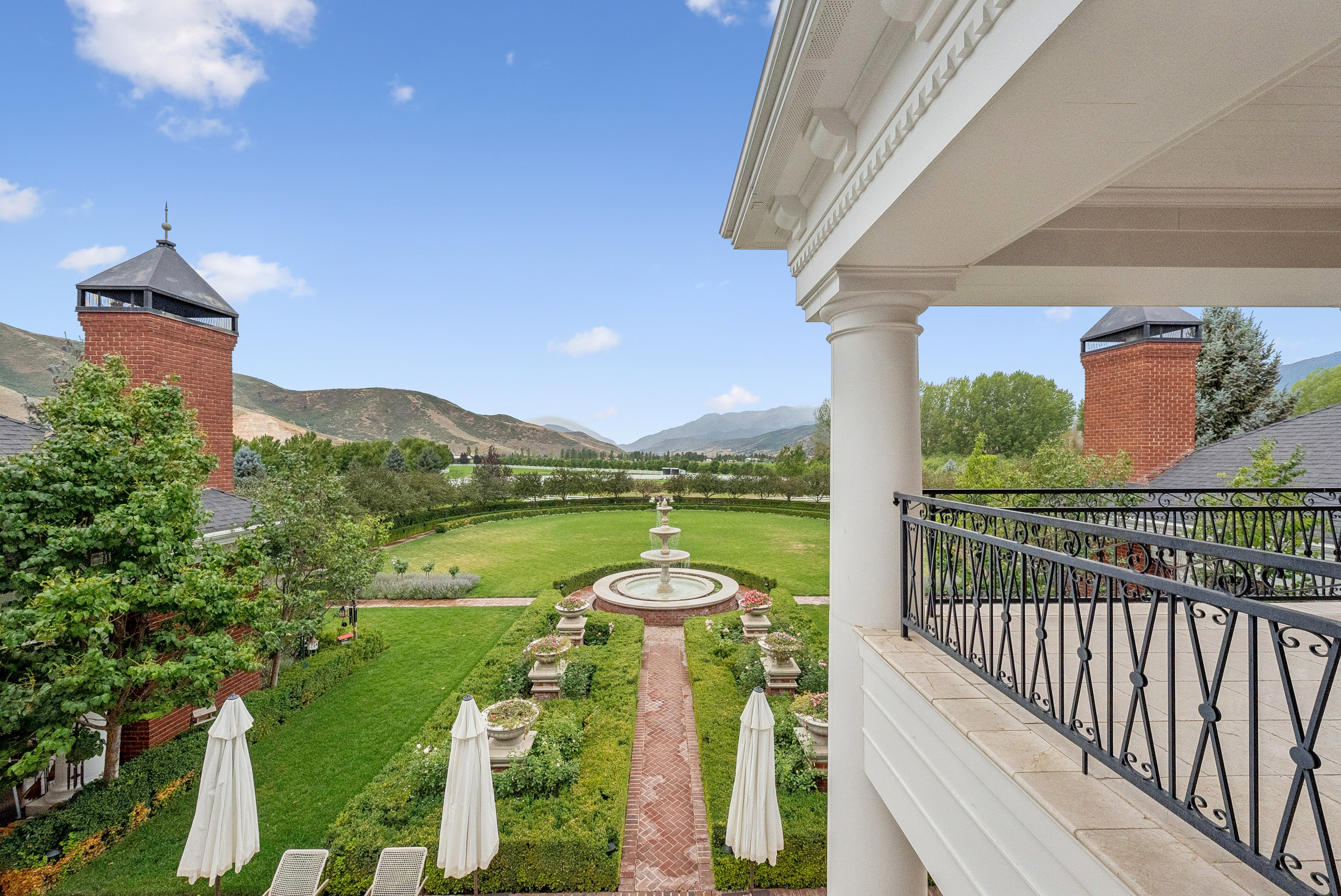 Expansive formal garden featuring a tiered fountain, intricate brick pathways, and manicured hedges