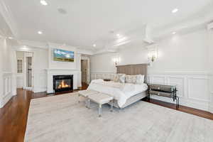 Bedroom with a fireplace with flush hearth, dark wood-style floors, recessed lighting, crown molding, and a decorative wall