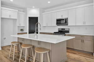 Kitchen featuring stainless steel appliances, recessed lighting, light wood-style floors, backsplash, and white cabinetry