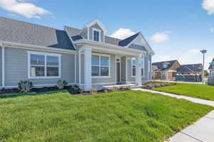 View of front of home with a porch, roof with shingles, and a front lawn