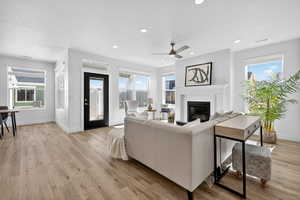 Living room featuring a glass covered fireplace, plenty of natural light, a ceiling fan, light wood-style flooring, and recessed lighting