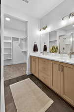 Bathroom featuring a walk in closet, double vanity, a stall shower, and recessed lighting