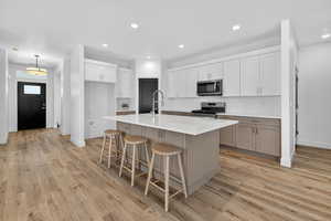 Kitchen featuring white cabinets, appliances with stainless steel finishes, a kitchen breakfast bar, an island with sink, and recessed lighting