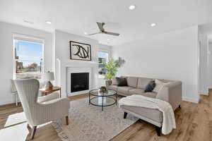 Living room featuring recessed lighting, light wood-style floors, a glass covered fireplace, and a ceiling fan