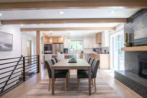Dining room with beam ceiling, light wood finished floors, recessed lighting, and a fireplace