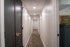 Corridor featuring dark colored carpet and recessed lighting
