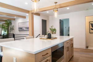 Kitchen with beam ceiling, light wood-style floors, hanging light fixtures, stainless steel microwave, and recessed lighting