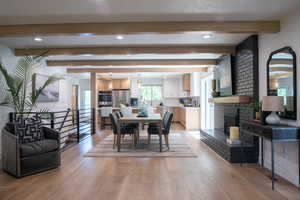 Dining space featuring beam ceiling, light wood-style flooring, recessed lighting, and a brick fireplace