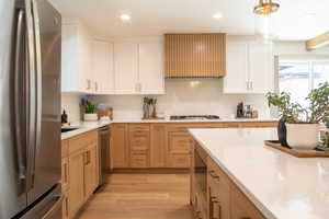 Kitchen with appliances with stainless steel finishes, light wood-style floors, light stone counters, white cabinets, and recessed lighting