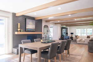 Dining room with light wood-style floors, beam ceiling, recessed lighting, and a fireplace