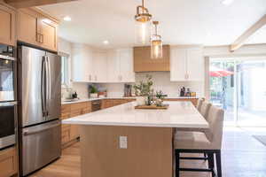 Kitchen featuring decorative light fixtures, appliances with stainless steel finishes, light wood-type flooring, light brown cabinetry, and a kitchen island
