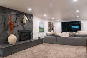 Living room featuring carpet, a stone fireplace, and recessed lighting