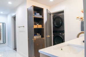 Laundry room with recessed lighting, estacked washer and dryer, and light marble finish floors
