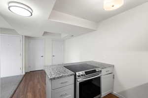 Kitchen featuring a peninsula, electric range, dark wood-style flooring, light stone counters, and white cabinetry
