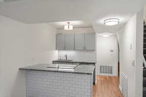Kitchen with decorative backsplash, a peninsula, light stone countertops, gray cabinets, and light wood-style floors