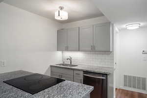 Kitchen featuring gray cabinetry, dishwasher, backsplash, light stone countertops, and dark wood finished floors