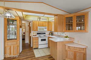 Kitchen featuring white appliances, glass insert cabinets, light countertops, a peninsula, and vaulted ceiling