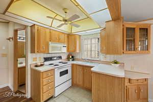 Kitchen with white appliances, light countertops, glass insert cabinets, and ceiling fan