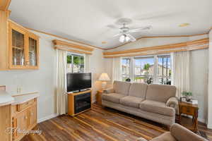 Living room with ceiling fan, dark wood-type flooring, vaulted ceiling, and crown molding