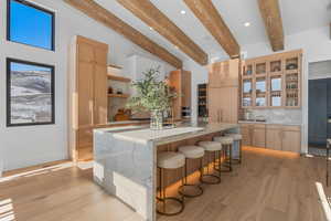 Kitchen with open shelves, a kitchen breakfast bar, light stone counters, backsplash, and beamed ceiling