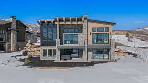 Snow covered back of property featuring stone siding, a patio, a mountain view, and a balcony