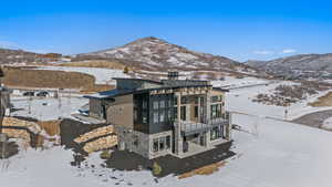 Snow covered rear of property featuring stone siding, a chimney, a balcony, a patio, and a mountain view