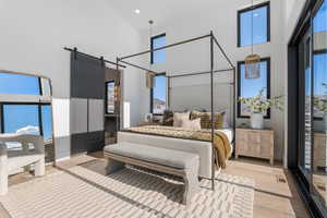 Bedroom featuring a barn door, a towering ceiling, multiple windows, wood finished floors, and recessed lighting