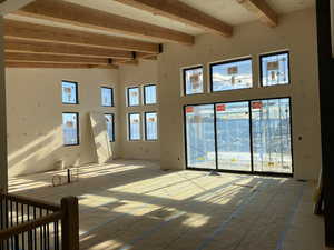 Unfurnished living room featuring beamed ceiling and a high ceiling