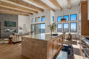 Kitchen featuring a towering ceiling, light wood-style floors, pendant lighting, light stone counters, and high end stove