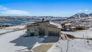 Modern home with a mountain view, a chimney, stone siding, an attached garage, and driveway