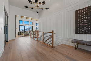 Hallway with an upstairs landing, a mountain view, light wood-type flooring, a chandelier, and a decorative wall