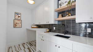 Kitchen with open shelves, decorative backsplash, white cabinets, and light stone countertops
