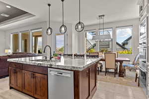 Kitchen with light stone countertops, stainless steel appliances, pendant lighting, a center island with sink, and open floor plan