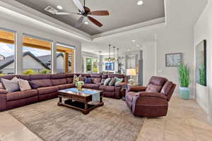 Living room with a tray ceiling, recessed lighting, ceiling fan, and light tile patterned floors