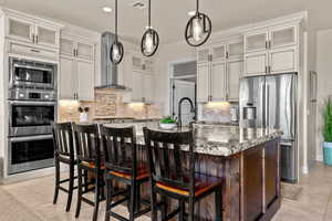 Kitchen with glass insert cabinets, backsplash, light stone countertops, appliances with stainless steel finishes, and a center island with sink