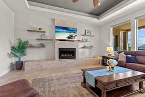 Living area with a raised ceiling, a fireplace, ceiling fan, and light tile patterned floors