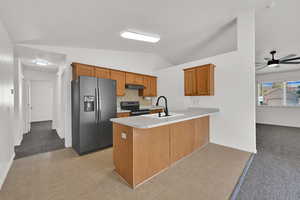 Kitchen with light colored carpet, brown cabinetry, stainless steel appliances, a peninsula, and vaulted ceiling