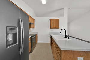 Kitchen with stainless steel appliances, a peninsula, brown cabinets, vaulted ceiling, and light countertops